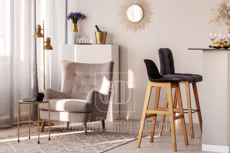 trendy grey armchair next to two black wooden bar stools in fashionable kitchen and dining room interior