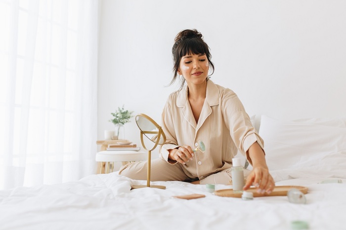 young,woman,sitting,on,bed,at,home,and,applying,cosmetics.